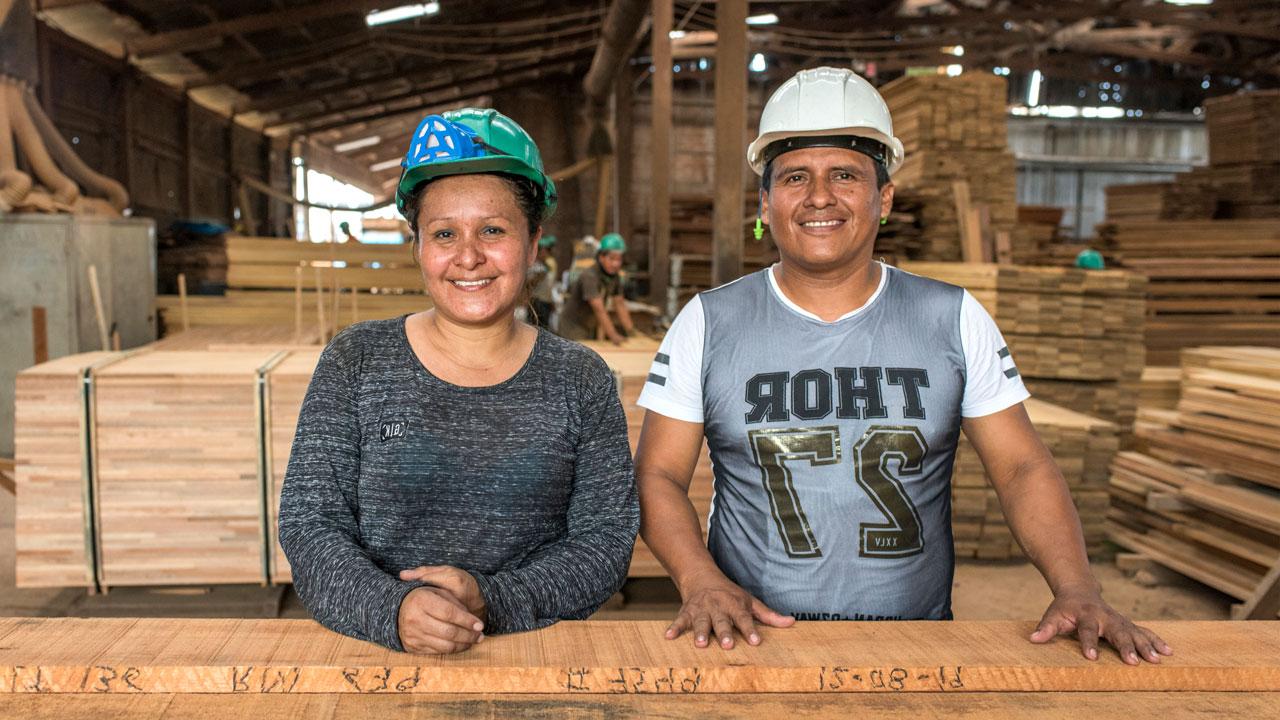 一名妇女和一名男子站在可持续生产的木材前，这是秘鲁利乐全球最大体育平台主导的林业项目的一部分
